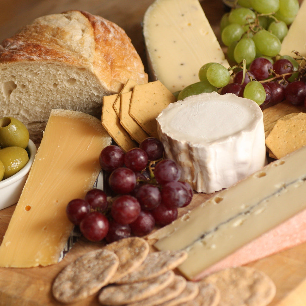 A variety of cheeses on cheese board with grapes, crackers and olives