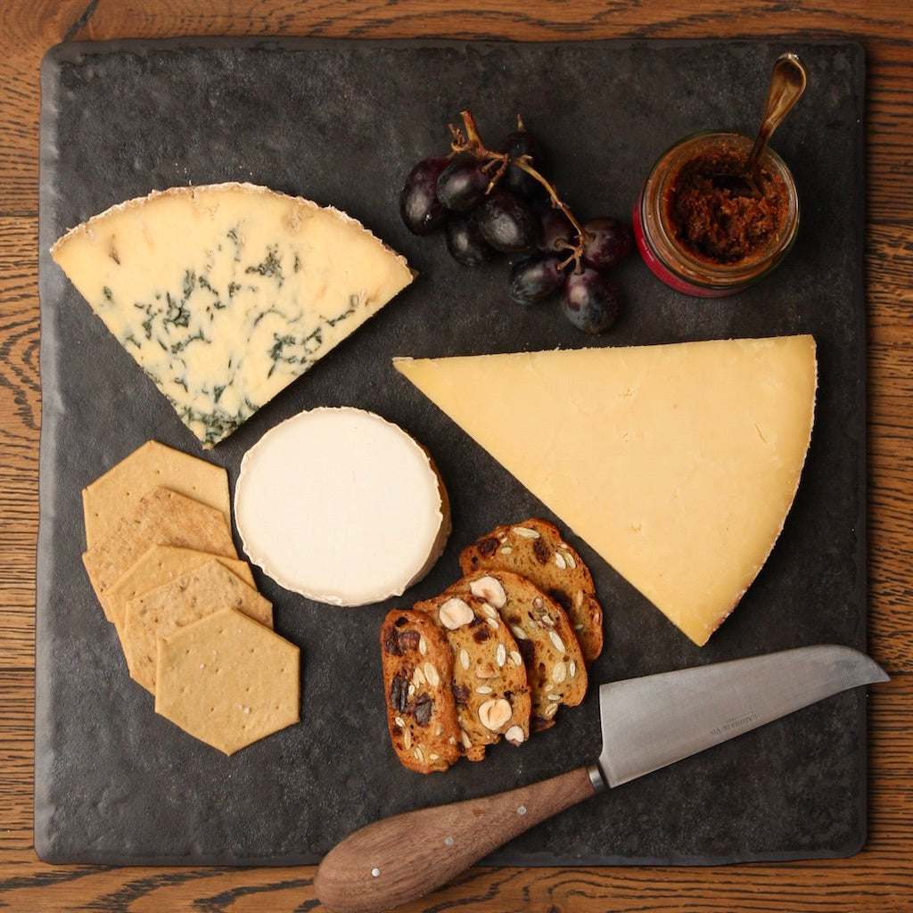 Cheeses on slate with knife, grapes & cheese crackers