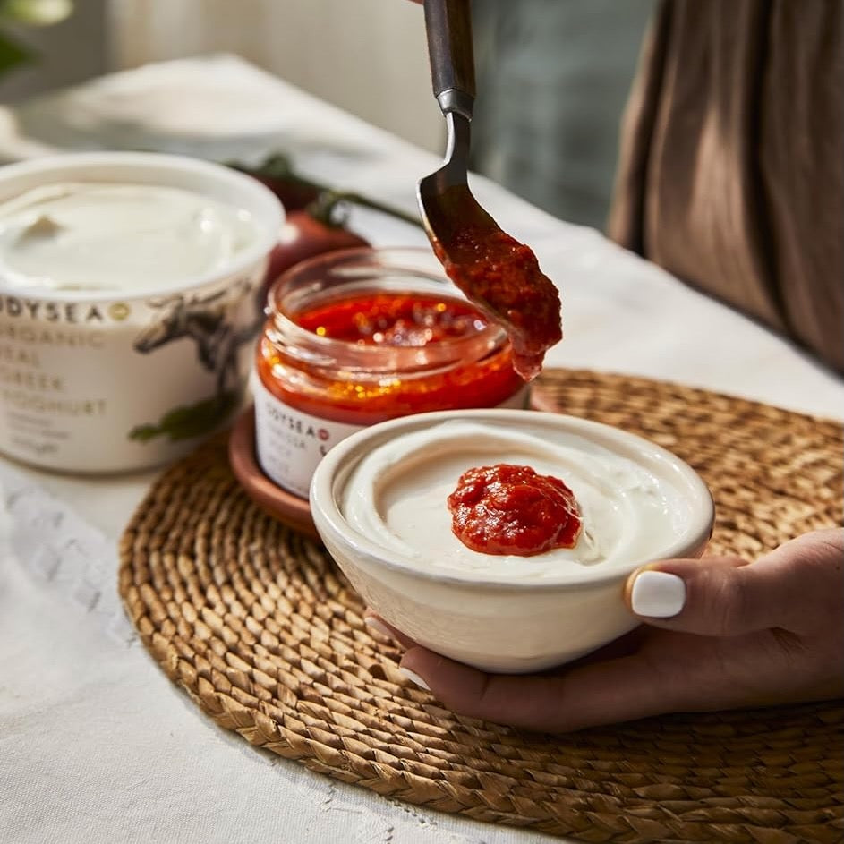 Person spooning harissa spicy meze onto a bowl of yogurt.