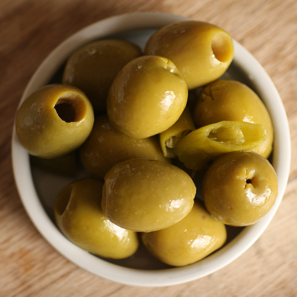White bowl filled with smoked green olives on a wooden surface