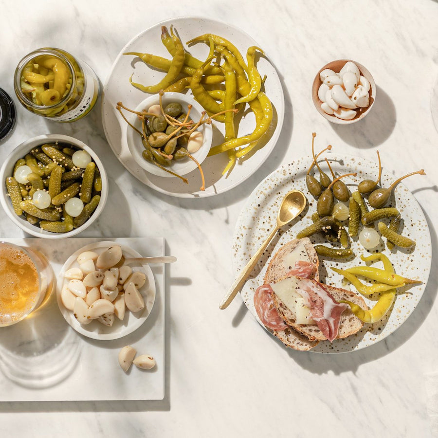 Assorted pickles and cured meats on a white surface with a glass of beer.