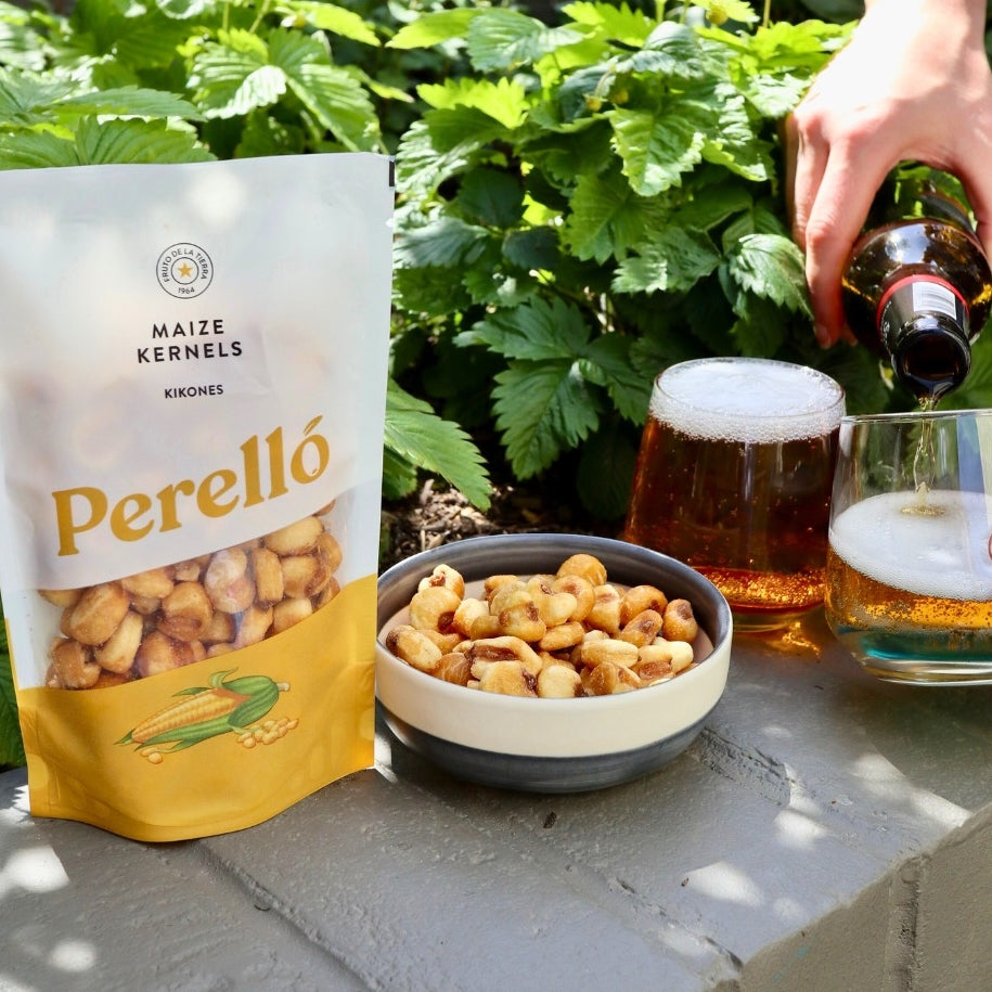 Bag of Perello maize kernels with a bowl and glass of beer on a stone surface outdoors.