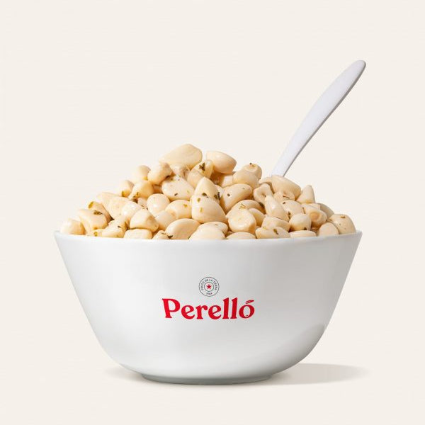 Bowl of Perello pickled garlic cloves with a spoon on a light background