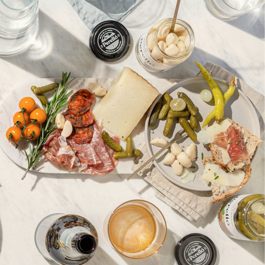 Plated appetizer with cured meats, cheese, pickles, and bread on a white marble surface.