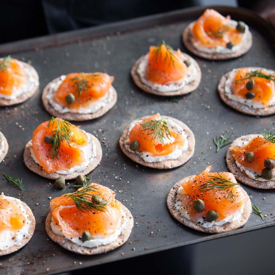 Tray of sourdough crackers topped with smoked salmon, cream cheese, and dill on a dark surface.