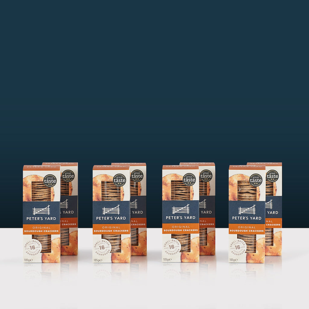 Multiple boxes of Peter's Yard sourdough crackers on a white surface with a dark blue background