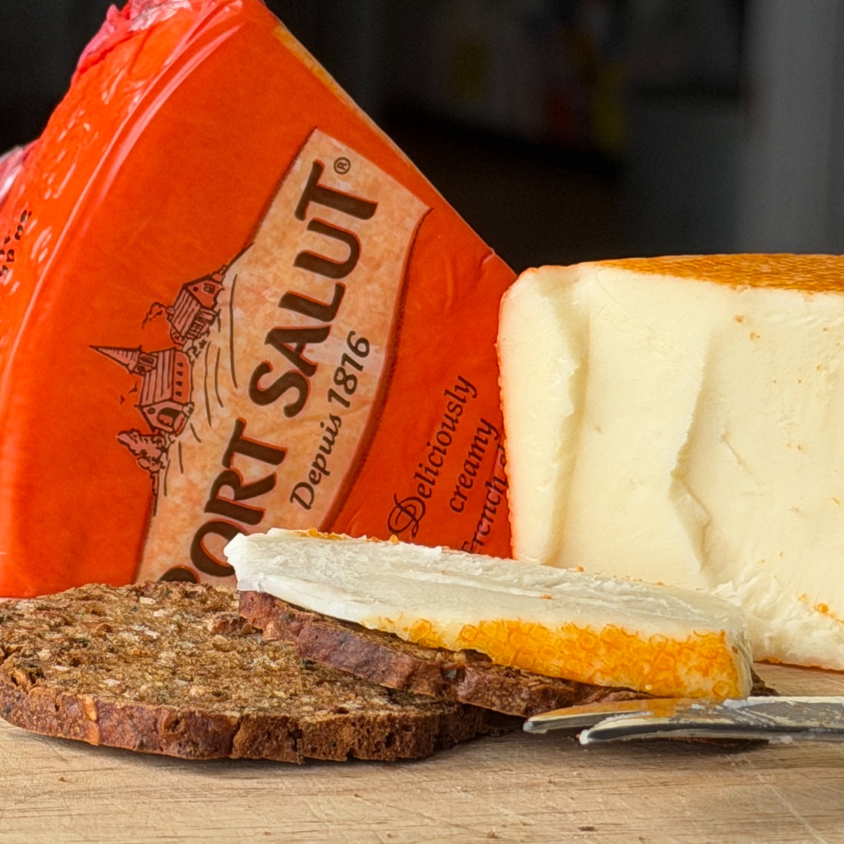Port Salut cheese with a slice cut off, served on a wooden board with bread.
