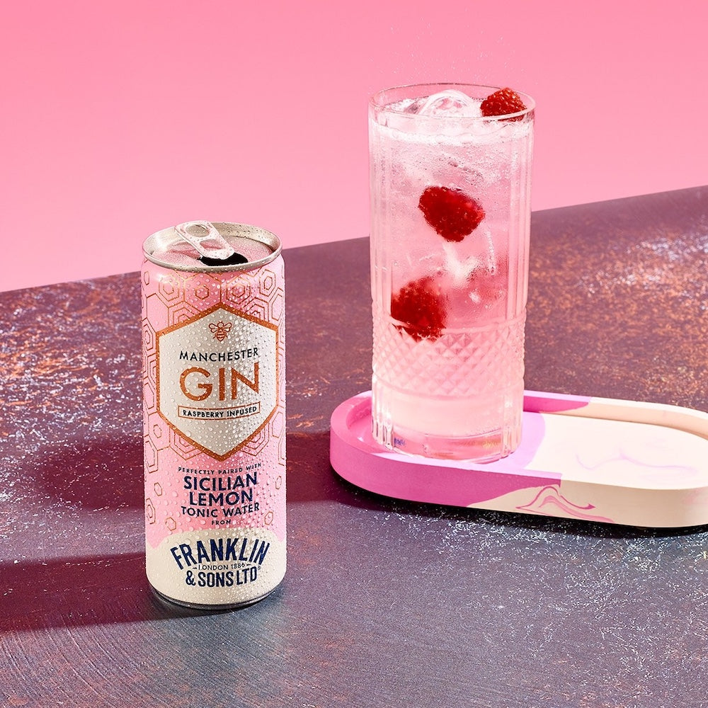 Can of Manchester Gin with a glass of pink cocktail with raspberries on a pink background
