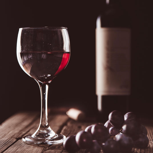 A glass of red wine with red grapes and a bottle of red wine