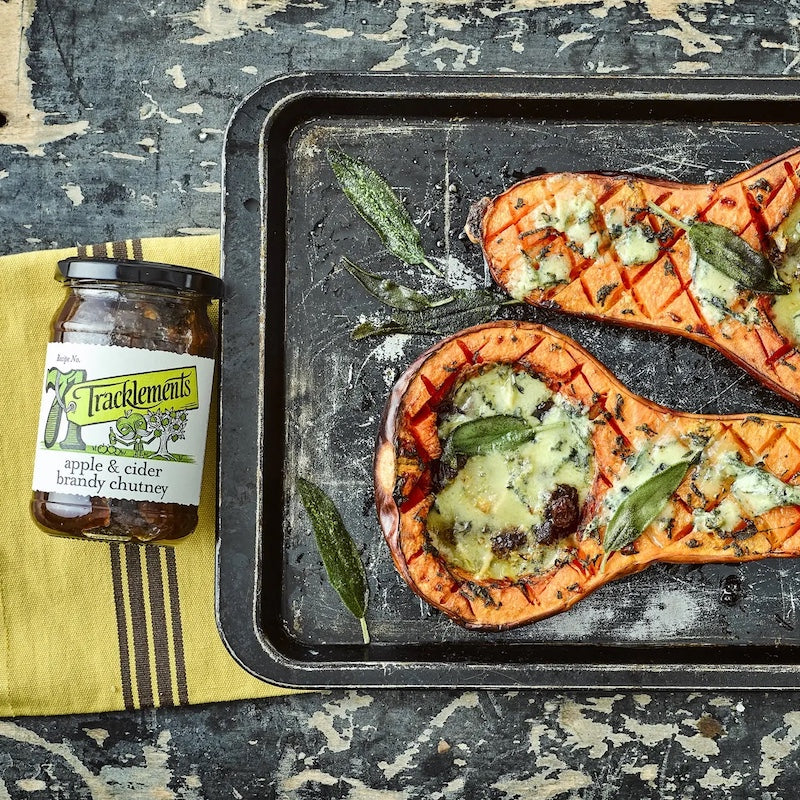 Baked squash with herbs and blue cheese on a tray next to a jar of Tracklement's apple & cider chutney.