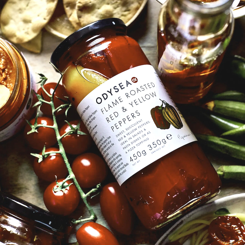 Odysea Flame Roasted Red Peppers jar on a table with tomatoes and other ingredients