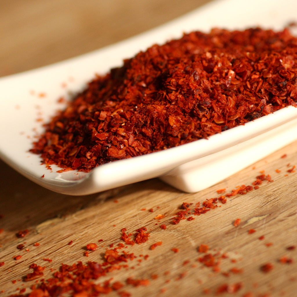 Smoked red chilli flakes on a white dish with some scattered on a wooden surface