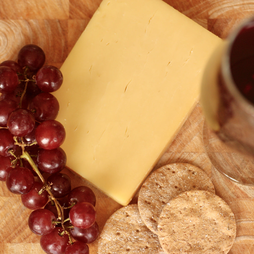 Smoked Cheddar, grapes, and crackers on a wooden board with a glass of red wine.