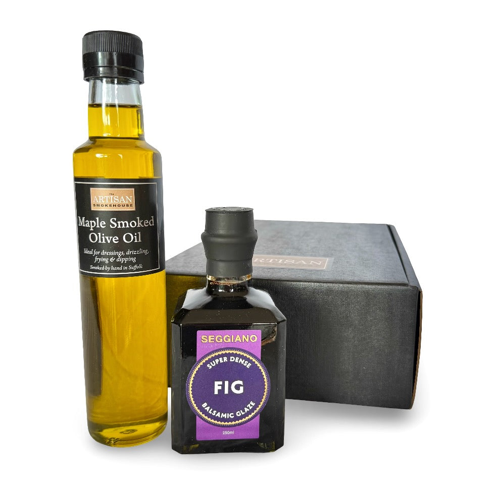 A gift set containing a tall bottle of Artisan Smokehouse Maple Smoked Olive Oil, a smaller bottle of Fig Balsamic, and a black presentation box on a white background.