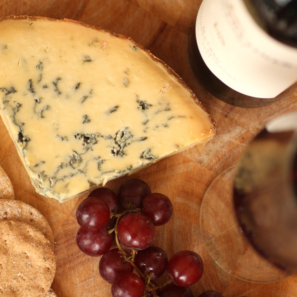 A piece of The Artisan Smokehouse's smoked Stilton on cheese board with a bottle of port