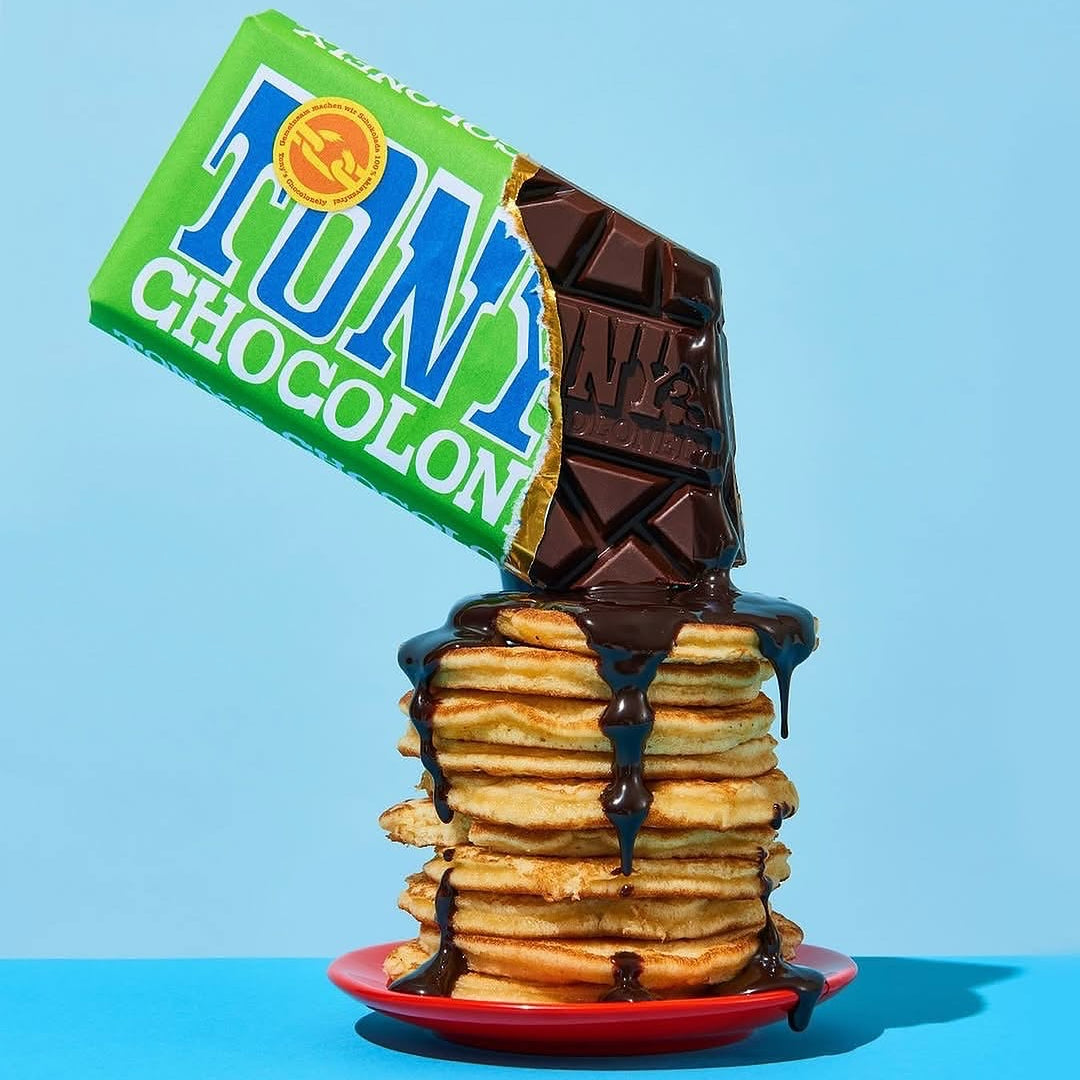 A stack of golden pancakes on a red plate, drizzled with Tony's Chocoloney dark chocolate