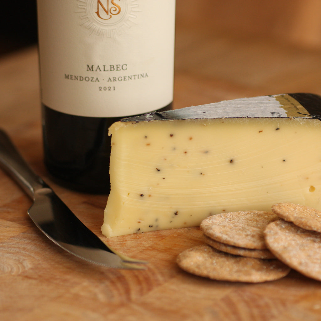 Bottle of Malbec wine with a wedge of Truffle Gouda and crackers on a wooden board