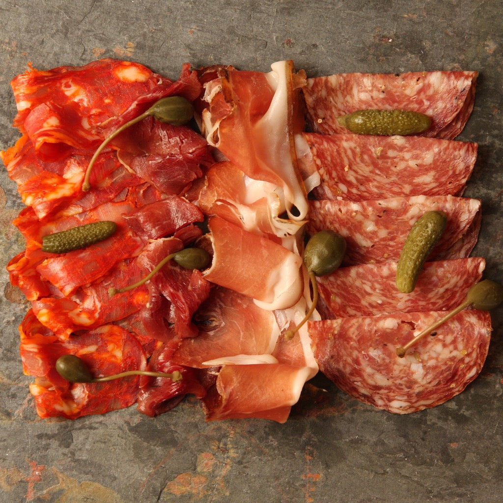 A platter of smoked sliced meats with pickled gherkins and capers