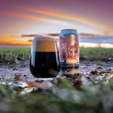 Glass of Big Sur Moon beer and can on grass with sunset in background