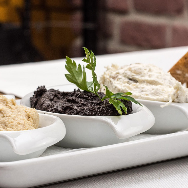 Assorted dips, including black olive paste, in small bowls on a platter