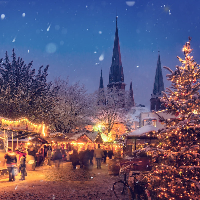 Snowy Christmas market with illuminated trees and buildings in the background