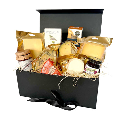 A luxury cheese gift hamper set in a black box with a black ribbon, filled with various cheeses, crackers, and preserves on a white background.