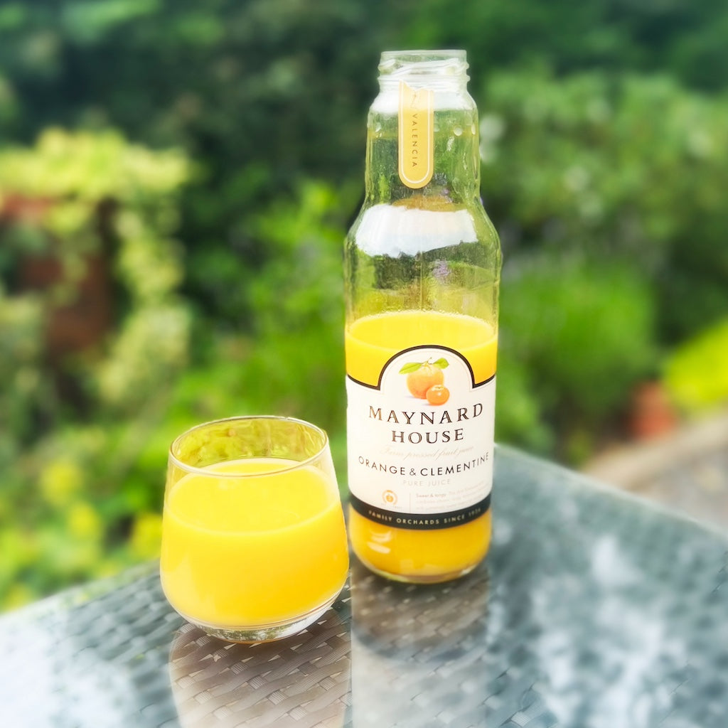 A bottle & glass of Maynard House orange and clementine juice on table