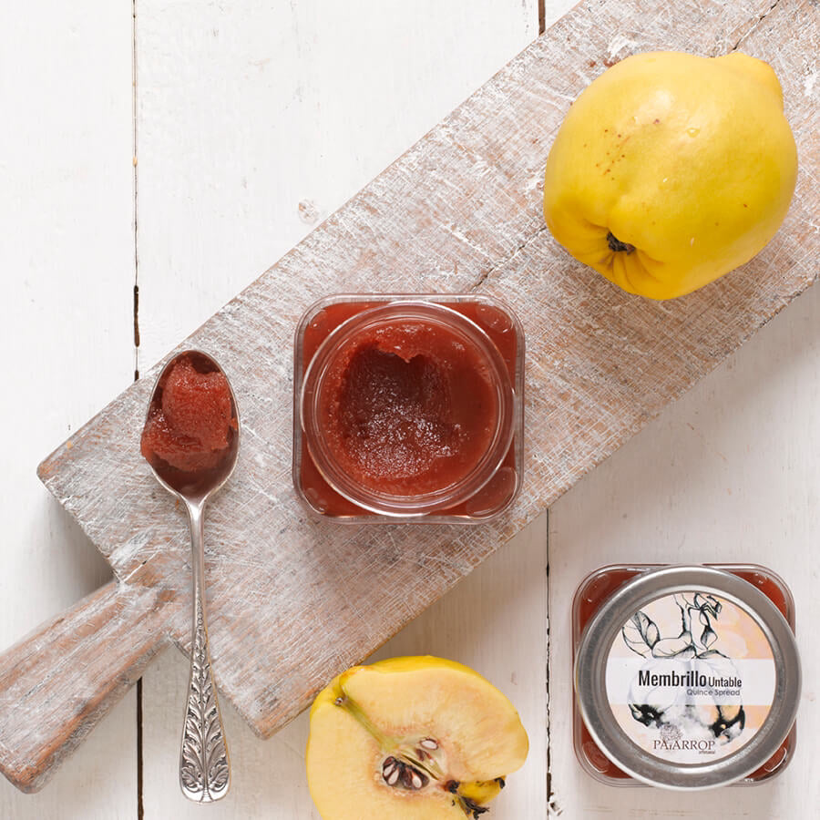 A jar of Membrillo quince jam on board with spoon and quinces