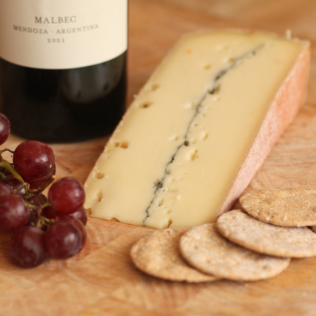 A piece of Morbier cheese on cheese board with wine, grapes and crackers