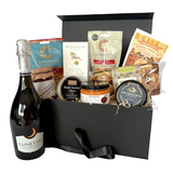 A gourmet gift hamper in a black box, featuring a bottle of Lunetta Prosecco, Cambrook corn, a jar of Odysea meze , a round cheese from Snowdonia, and other packaged snacks and sweets, arranged in a black gift box.