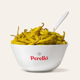 Bowl of pickled Guindilla peppers with a white spoon on a light background, featuring the Perello brand.