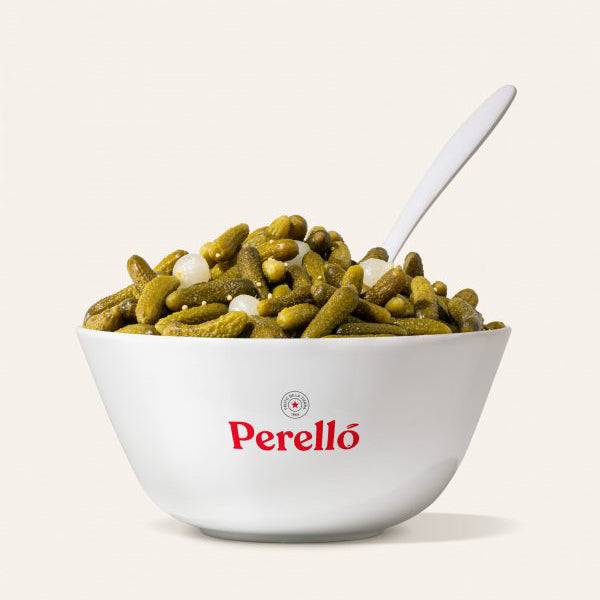 Bowl of Perello cocktail gherkins with a spoon on a white background, featuring the Perello brand.