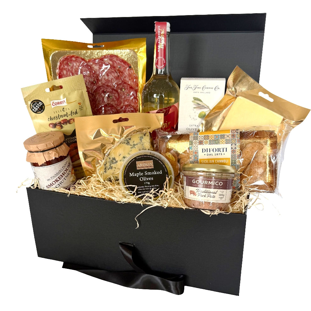 A gourmet picnic hamper filled with assorted cheeses, cured meats, crackers, and a bottle of drink, arranged inside an open black gift box.