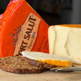 Port Salut cheese with a slice cut off, served on a wooden board with bread.