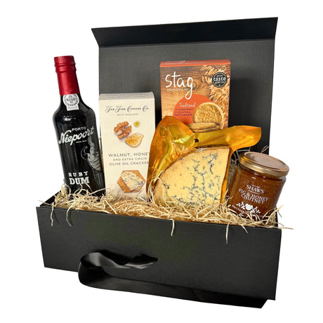 A gourmet cheese and Port gift hamper in a black presentation box filled with wood wool. The set includes a bottle of Ruby Dum Port, crackers, a block of blue cheese in gold foil, a jar of Fig & Honey chutney, and a box of Stag Traditional oatcakes.
