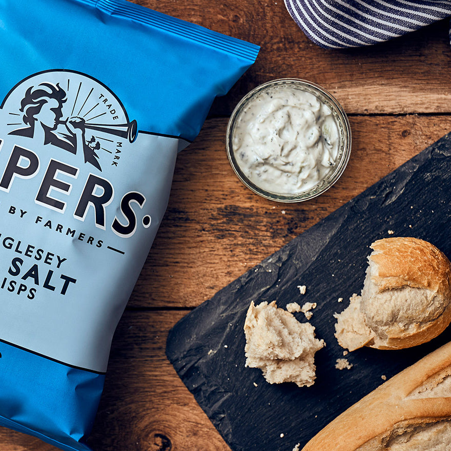 A packet of artisan crisps on a table with fresh bread and dips