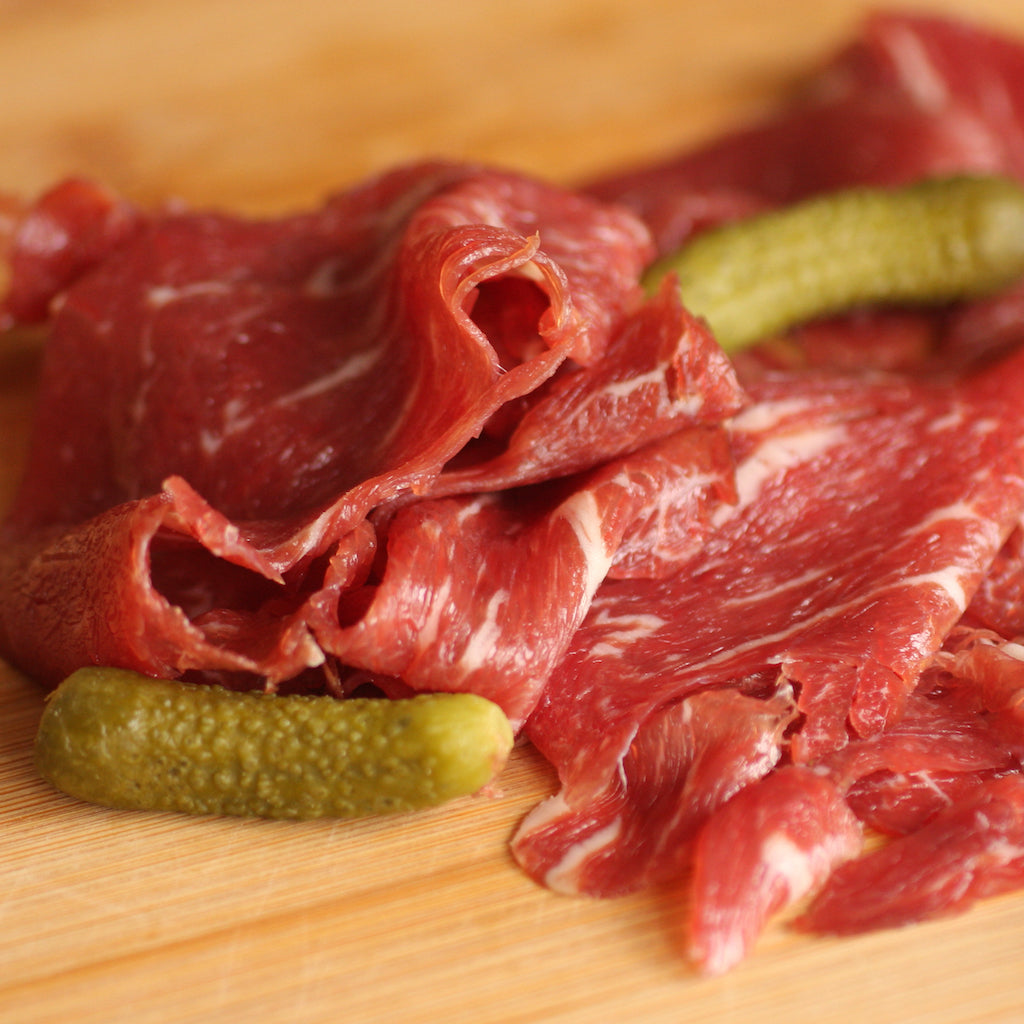 Slices of The Artisan Smokehouse's smoked beef fillet on wooden board with cornichon