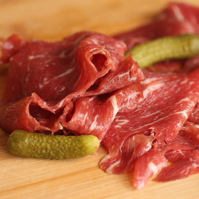 Sliced of smoked beef fillet with pickles on a wooden board