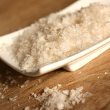 Coarse smoked sea salt crystals piled in a white rectangular dish on a wooden surface.
