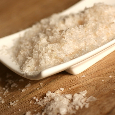 Coarse smoked sea salt crystals piled in a white rectangular dish on a wooden surface.