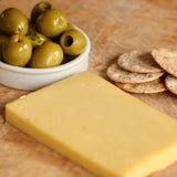 Block of smoked cheese with a bowl of green olives and crackers on a wooden surface