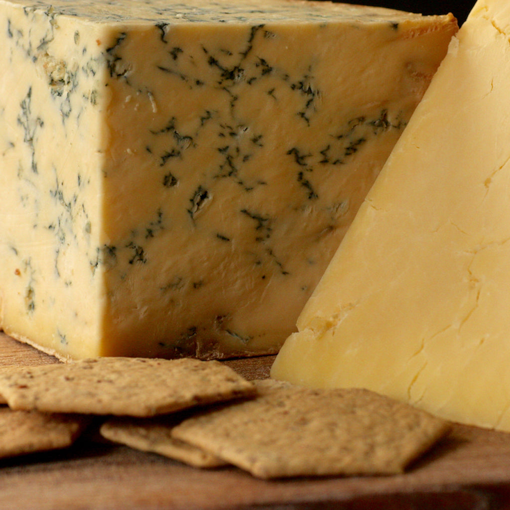 A block of smoked Stilton and smoked Cheddar on a cheese board with crackers 