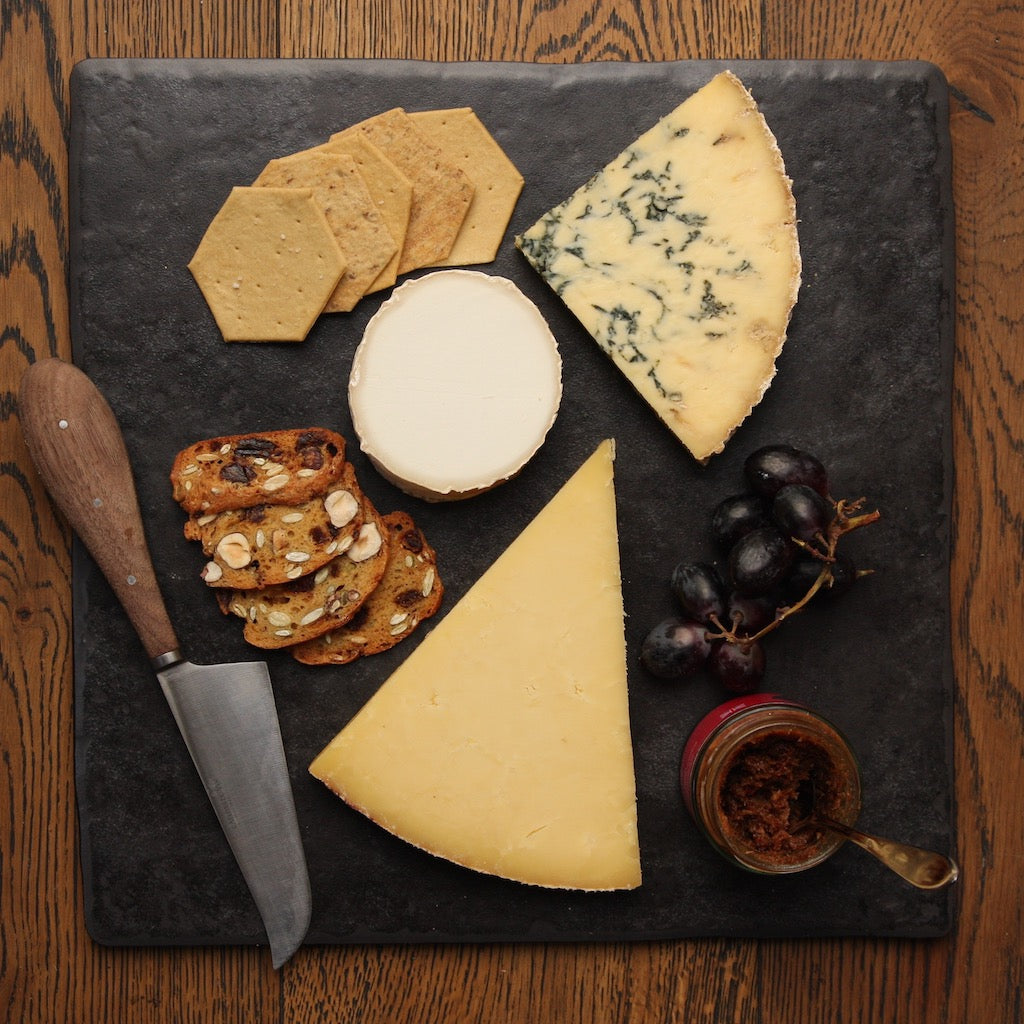 Pieces of The Artisan Smokehouse's smoked Stilton, Cheddar and goat on a slate with crackers and chutney