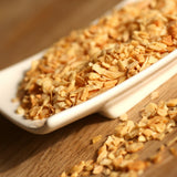 Dried smoked garlic granules in a white rectangular dish on a wooden surface, with some scattered in the foreground.