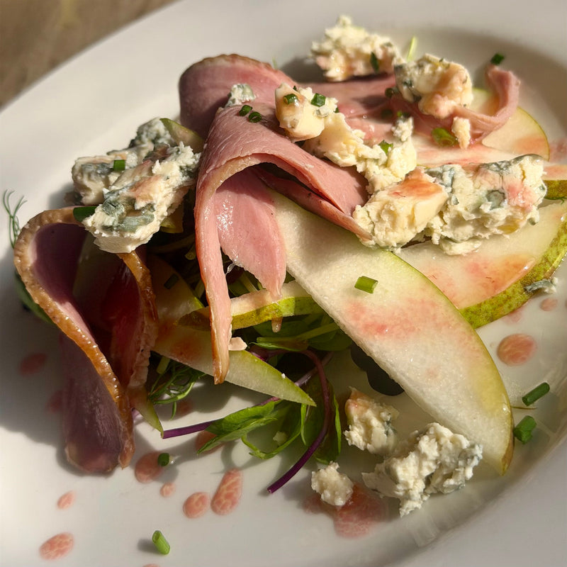 Slices of smoked duck on a blue cheese salad with pear