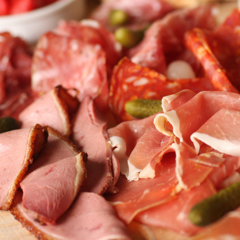 Slices of The artisan Smokehouse's smoked meats on a meat platter with cornichon