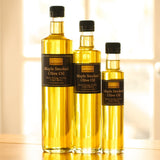 Three bottles of Maple Smoked Olive Oil in different sizes, standing on a wooden surface.