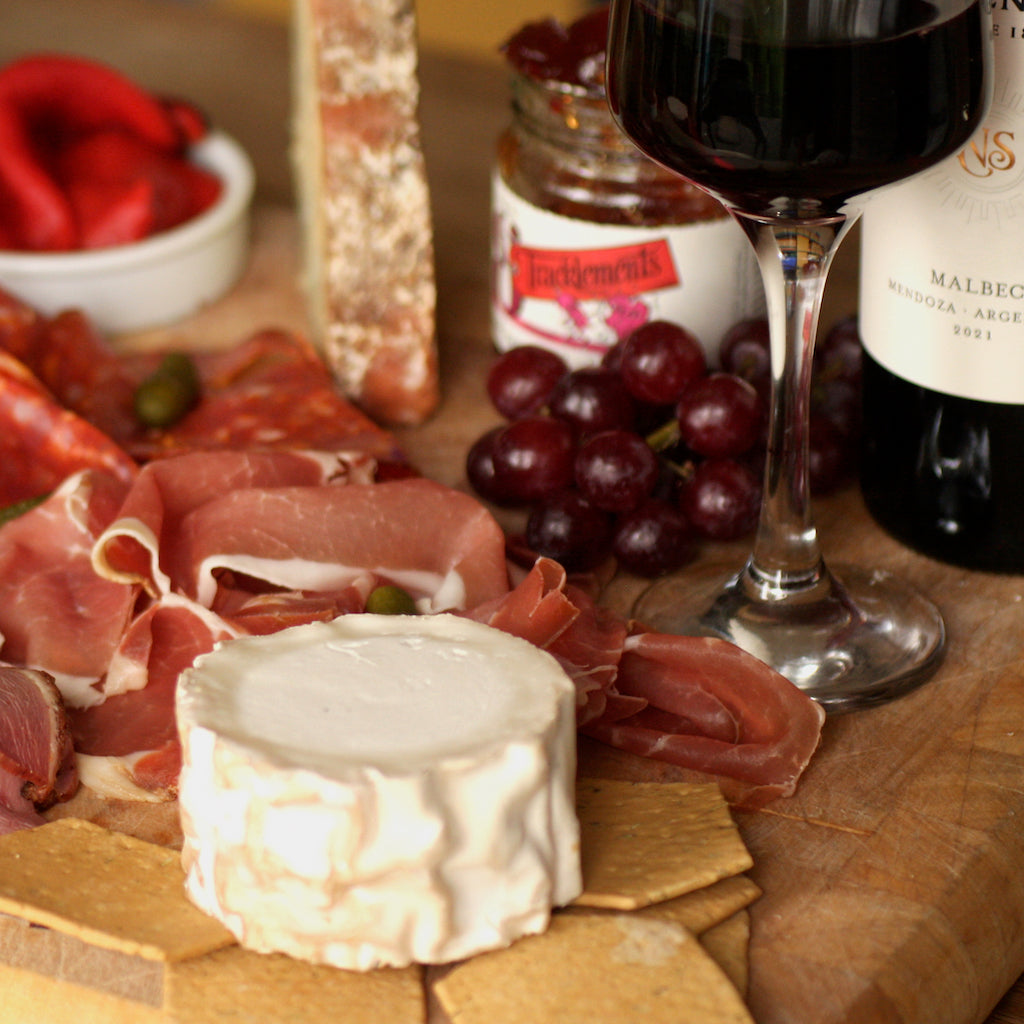 A selection of The artisan Smokehouse's smoked meats on platter with smoked cheese and a bottle of Malbec wine