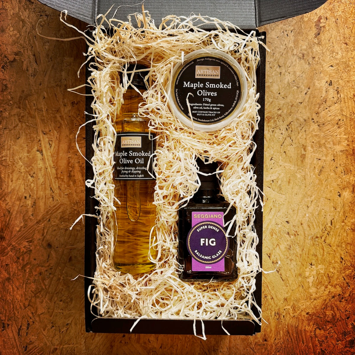 A black box containing smoked olive oil, Fig balsamic glaze and a pot of smoked olives.