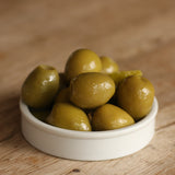 Green smoked olives in a white bowl on a wooden surface